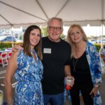 Three adults pose together under a white tent at an outdoor event, with tables, chairs, and wine bottles visible in the background at the SB Sculpture gathering.