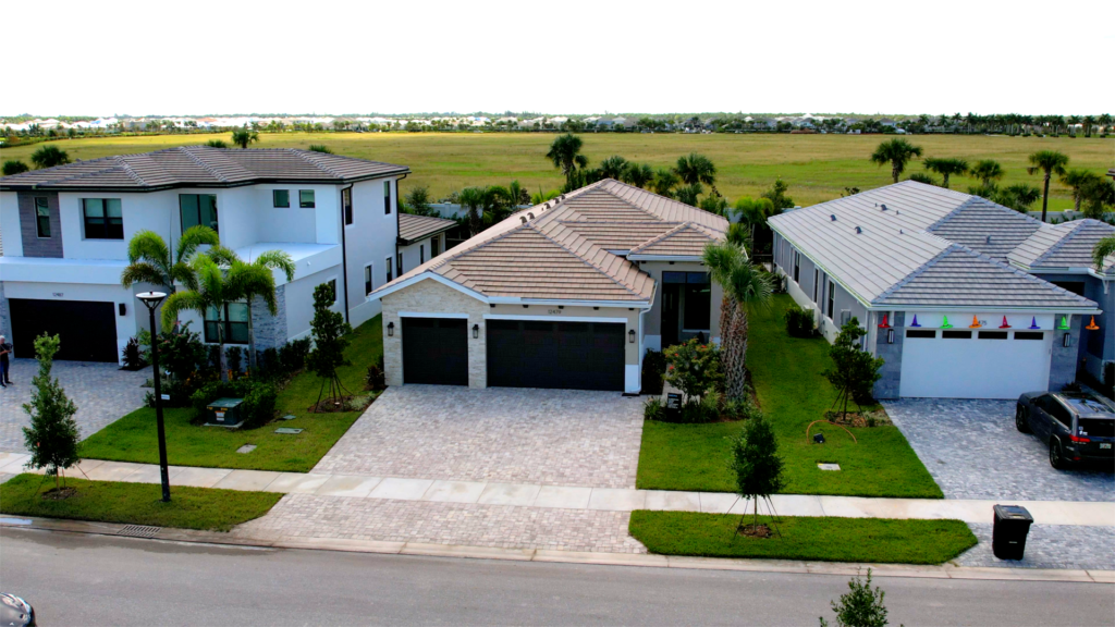 A row of modern suburban houses with well-maintained lawns, driveways, and garages, set against an open grassy field—select homesites available with no CDD debt, offering you the chance to save thousands.