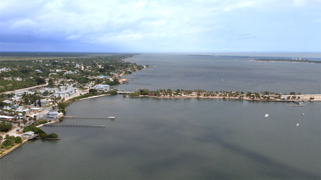 Aerial view of Catalina Palms in Port St. Lucie, a coastal town featuring houses, docks, and a bridge over calm water—an inviting setting ideal for 55+ buyers seeking serene waterfront living under a partly cloudy sky.