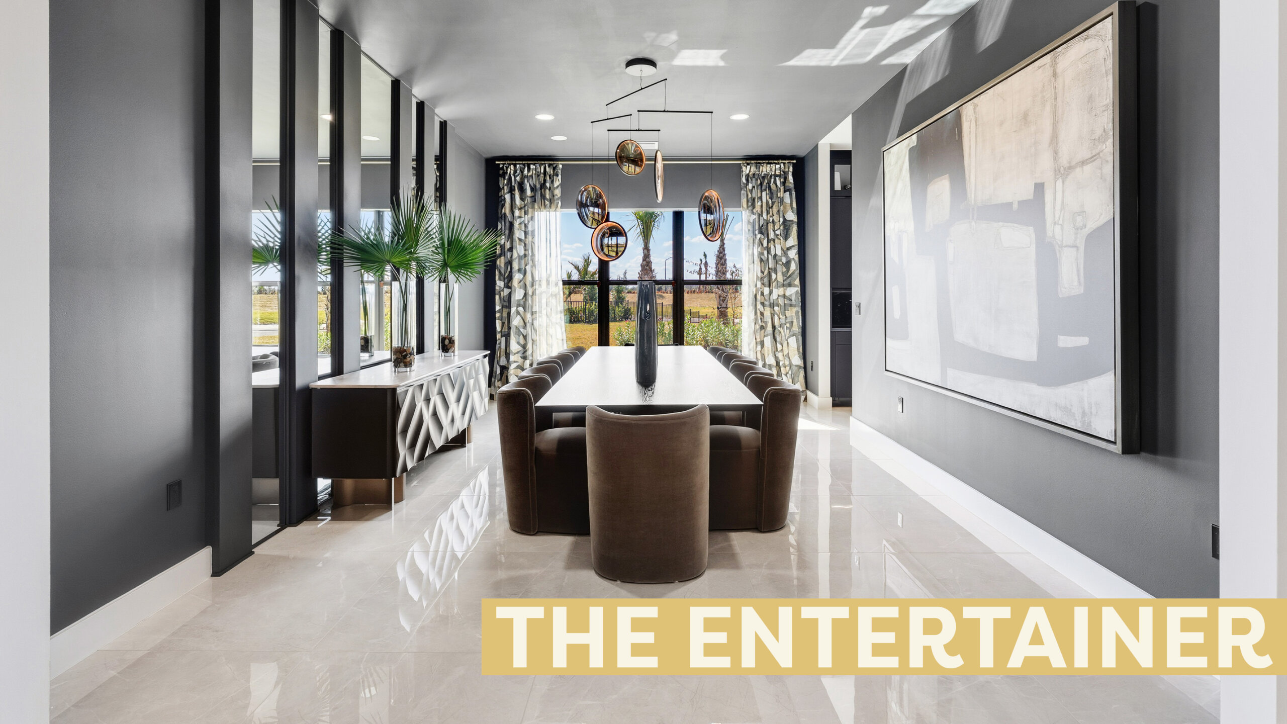 Modern dining room in the Catalina Palms home with large windows, a rectangular table for eight, abstract wall art, and decorative plants. Text overlay reads "THE ENTERTAINER. Find your perfect gathering space here.